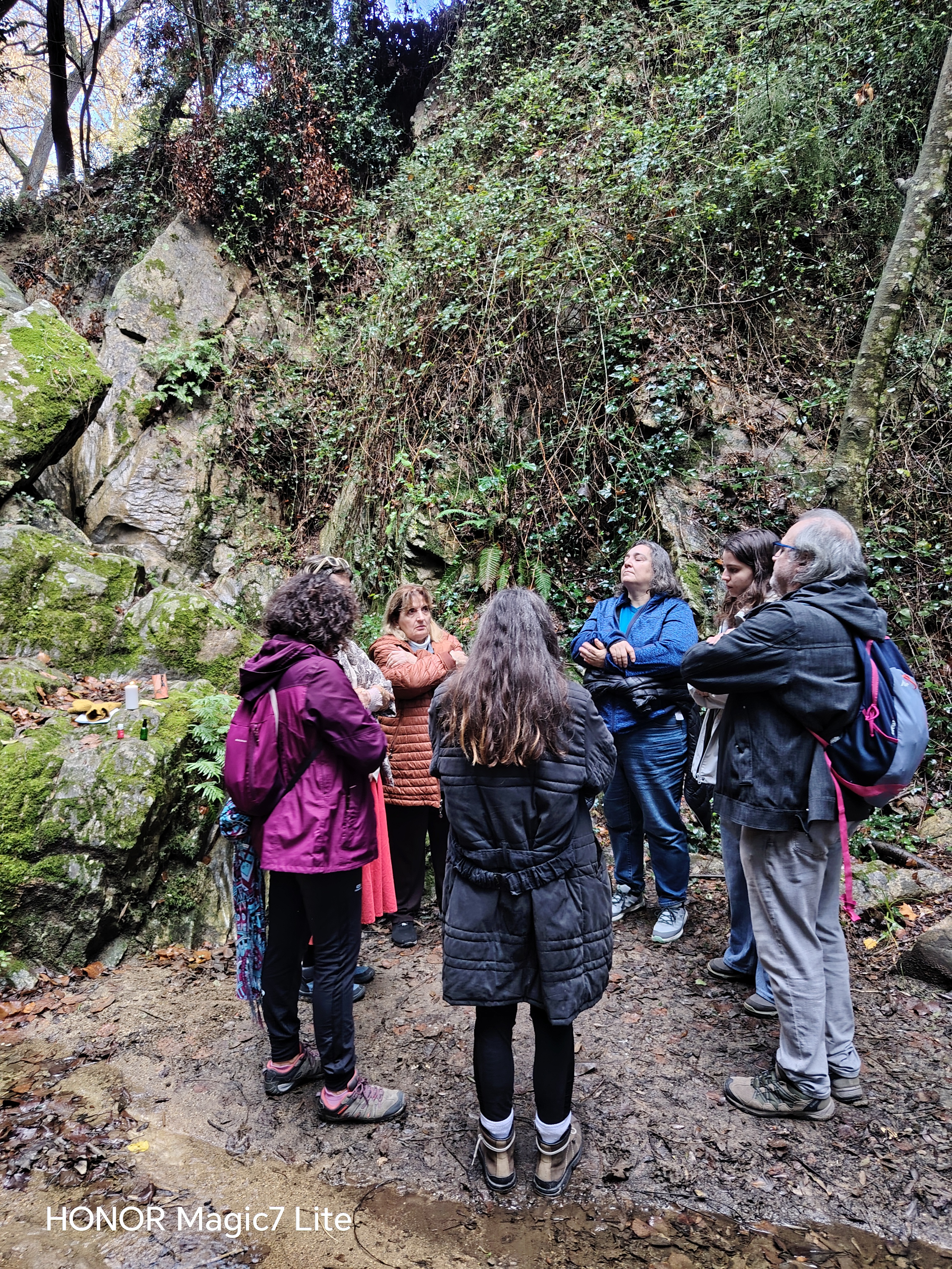 Grupo reunido en círculo frente a un pequeño altar entre grandes rocas cubiertas de musgo durante una paseada aromática de invierno